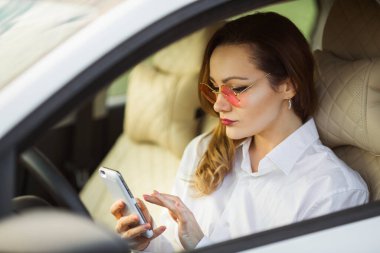 Güzel genç bir kadın cep telefonuyla araba kullanıyor.