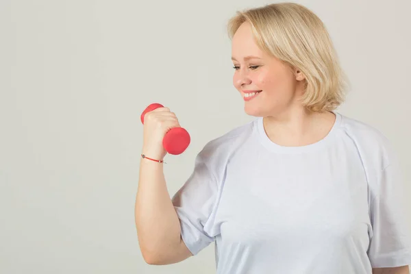 beautiful young plump woman in a white t-shirt on a white background with dumbbells