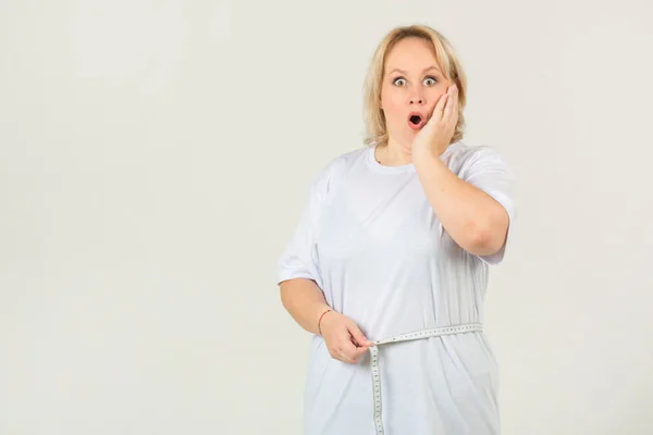 beautiful young plump woman in a white t-shirt on a white background measures the volume of her body with a measuring tape