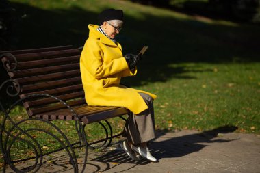 Sonbaharda parkta gözlüklü bir kadın cep telefonuyla.