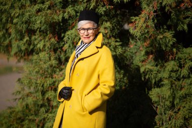 Sonbaharda parkta sarı ceketli yetişkin bir kadın.