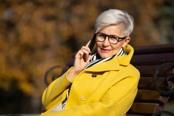 Dorosła Kobieta Wieku Siedzi Ławce Telefonem Komórkowym Rękach Jesienią Parku — Zdjęcie stockowe