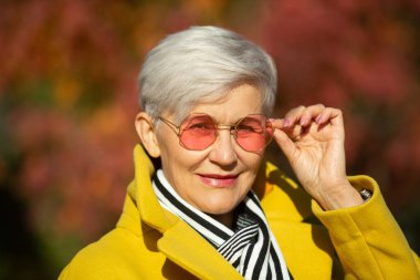 Sonbaharda parkta sarı ceketli yetişkin bir kadın.