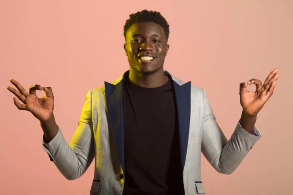 portrait of handsome african man in suit on pink background with hand gesture