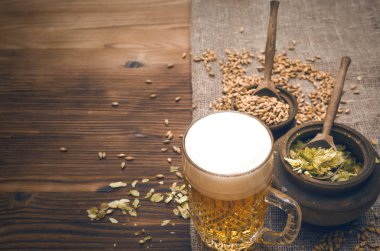 Soğuk köpük bira malt tahıl ile yeşil hop tencere ve çavdar kulaklar kahverengi ahşap masa arka plan üzerine çuval bezi kumaş yaprak.