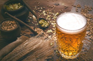 Soğuk köpük bira malt tahıl ile yeşil hop tencere ve çavdar kulaklar kahverengi ahşap masa arka plan üzerine çuval bezi kumaş yaprak.