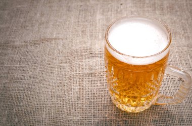 Çuval bezi arka plan üzerinde köpüklü light bira bardak.