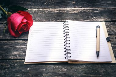 Kırmızı gül çiçek ve yaşlı ahşap masa arka plan üzerinde boş sayfaları ile not etmek. Tebrik kartı tasarımı.