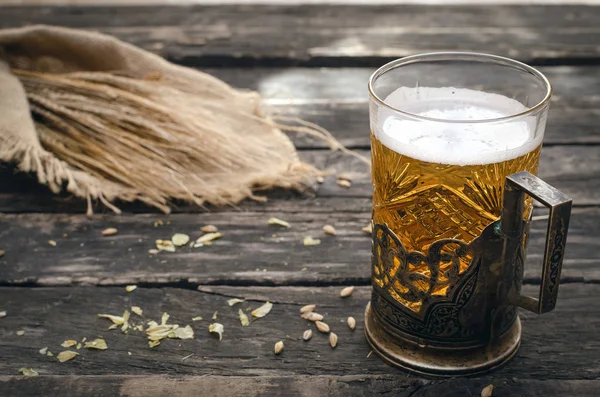 stock image Glass of light beer with scattered around hop and malt and rye ears on aged wooden table background.