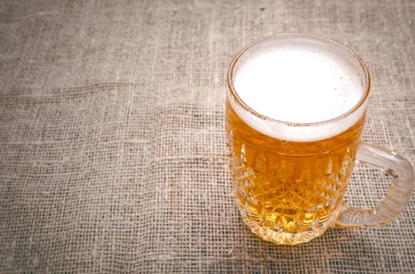 Çuval bezi arka plan üzerinde köpüklü light bira bardak.