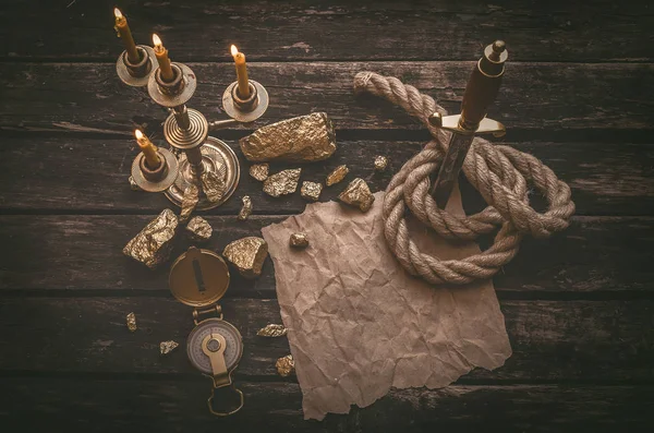 Pirate gold and treasure map crumpled parchment with copy space, dagger, compass and ship rope on old table background.