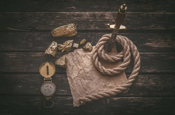 Pirate gold and treasure map crumpled parchment with copy space, dagger, compass and ship rope on old table background.