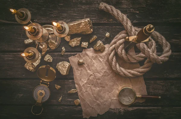 Pirate gold and treasure map crumpled parchment with copy space, dagger, compass and ship rope on old table background.