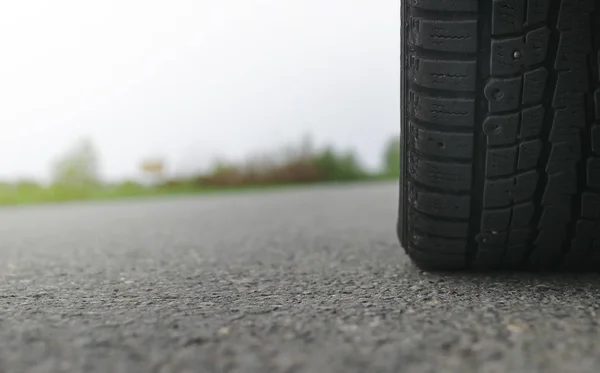 Car tyre close up on the empty asphalt road in the cloudy rainy day with copy space. Car travel concept.