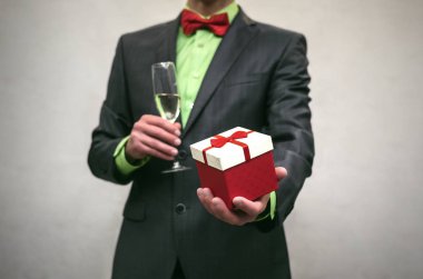 Takım elbiseli adam bir elinde bir hediye kutusu ve şampanya bardağı beyaz izole başka bir elinde tutar. Ödül töreni.