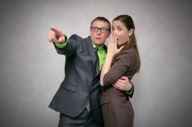 Shocked and frightened business couple looking ahead isolated on gray background. Telling the secrets concept. The lies. clipart