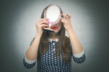Kadın kız aynaya baktığında, kalıcı makyaj ve gri arka plan üzerinde izole pretties yapmaz. Bir tarih kavramı için hazırlanıyor.