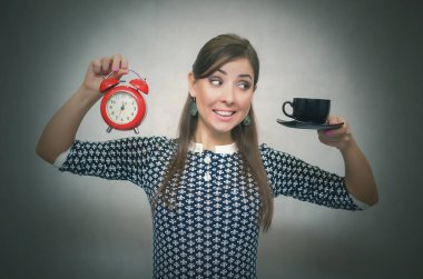Kahve molası. Kahve zamanı. Öğle yemeği molası. Bir gri arka plan üzerinde izole saat ile bir fincan kahve ve kırmızı alarm clock elinde tutan mutlu gülümseyen kadın.