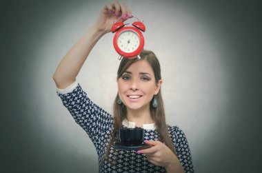 Kahve molası. Kahve zamanı. Öğle yemeği molası. Bir gri arka plan üzerinde izole saat ile bir fincan kahve ve kırmızı alarm clock elinde tutan mutlu gülümseyen kadın.