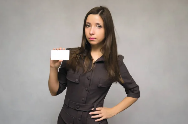Serious business woman holds in one hand a blank visit card with copy space and holds a belt  by another hand. Contact us.