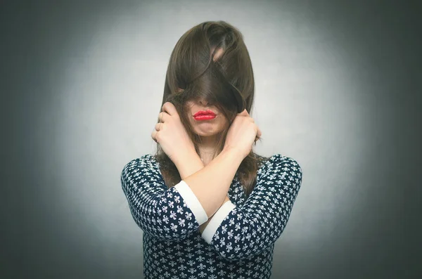 Offended woman hides her face behind her hairs isolated on gray background. Incognito. Faceless person.
