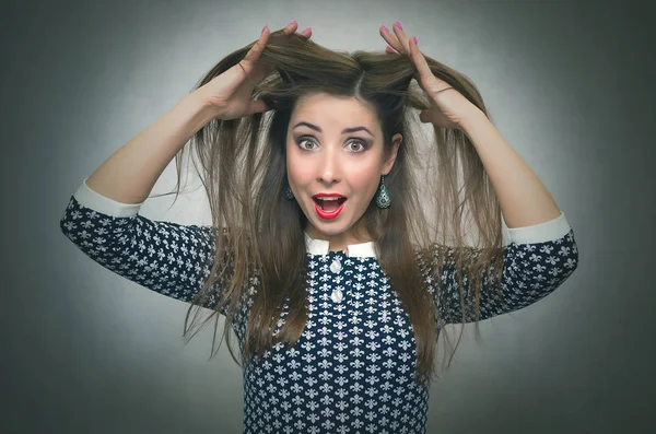 Surprised woman in shock is holding her hair on a head by her hands and is screaming isolated on gray background. Suddenness. Win.