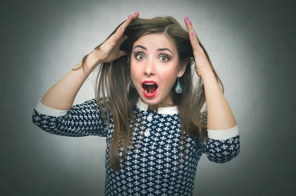 Surprised woman in shock is holding her hair on a head by her hands and is screaming isolated on gray background. Suddenness. Win.