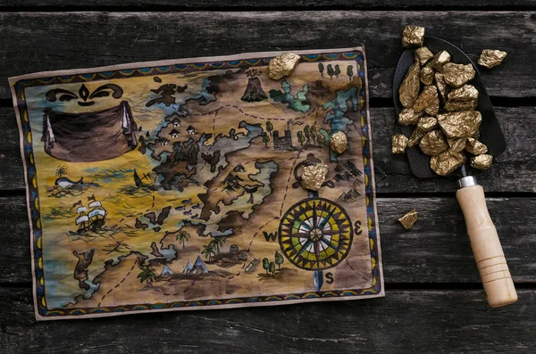 Treasure map and shovel full of gold nuggets ore on wooden table. Treasure hunter or gold miner concept.