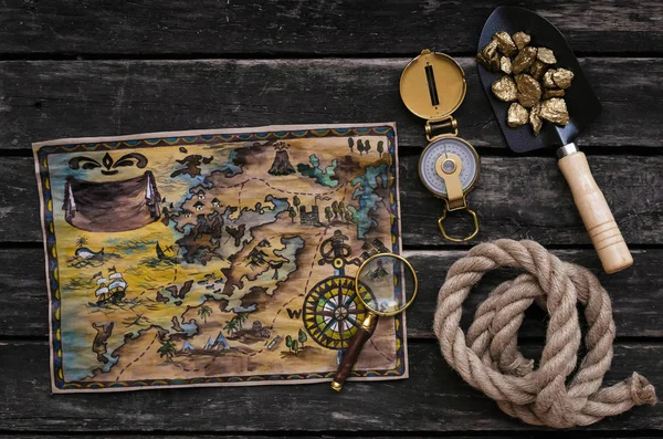 Treasure map, shovel full of gold ore, compass, rope and magnifying glass on aged wooden table background. Treasure hunter concept.