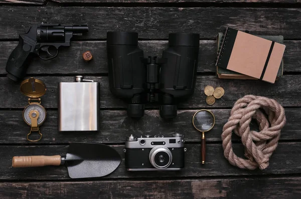 Compass, binoculars, film photo camera, loupe, handgun, diary book, shovel, rope, hat and gold ore on adventurer or explorer wooden table. Traveler equipment.