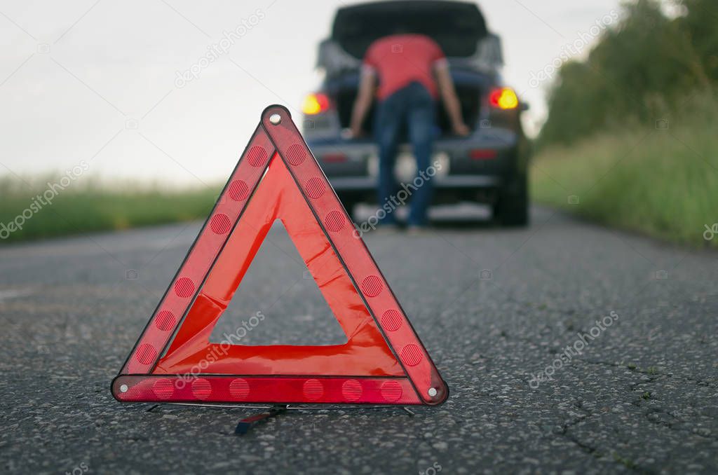 Car breakdown. Red emergency triangle stop sign and driver near car background.