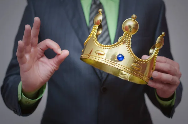 Businessman king holding in hands a gold crown and showing okey sign. Award ceremony concept. Winner.