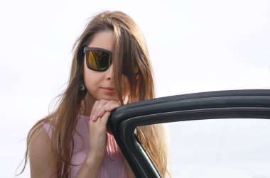 Genç kadın kahverengi uzun saçlı ve arabanın kapısını hakkında duran güneş gözlüğü ve arıyor.