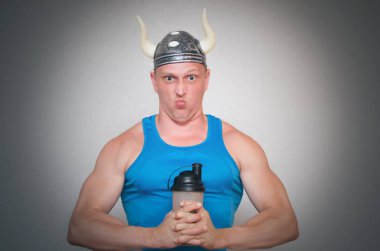 Vücut geliştirmeci erkek boynuzlu viking şapkalı yeni protein elinde gri arka plan üzerinde izole kokteyl gelen vahşi olacak.