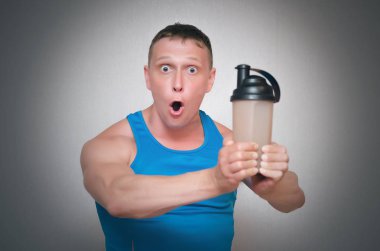 Vücut geliştirmeci adam yeni protein kokteyl içme o gri arka plan üzerinde izole dan sürpriz.