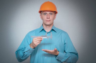 Oluşturucu işçi gri arka plan üzerinde izole onun elinde bir kumpas kullanarak ölçer.