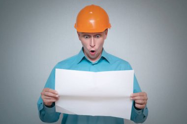 Geniş açık ağızlı gri arka plan üzerinde izole bir ev proje planı şok Oluşturucusu çalışan adam hoilding eller.