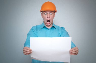 Şok Oluşturucusu inşaat işçisi gri arka plan üzerinde izole bir planı taslağı belgesini elinde tutuyor.