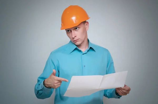 Verwirrter Bauarbeiter Hält Auf Grauem Hintergrund Einen Planentwurf Der Hand — Stockfoto