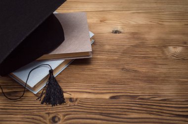 Graduate cap and stack of books on the wooden school desk with copy space. clipart