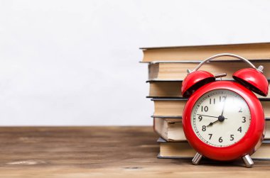 Yığın kitap ve beyaz arka plan üzerinde izole okul masasında kırmızı çalar saat.