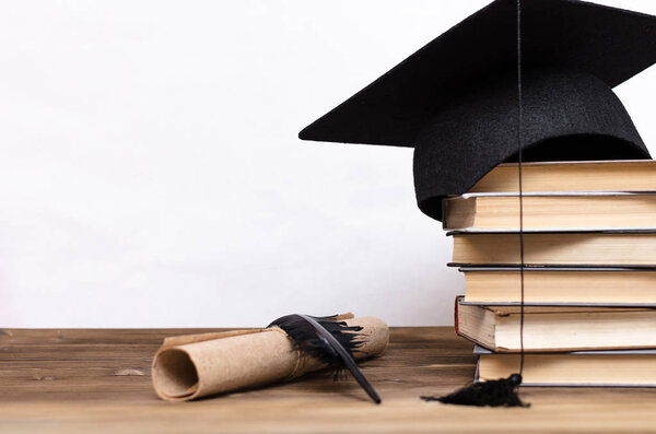 Stack of books, graduate cap, diploma and fether pen on the school desk isolated on white background.