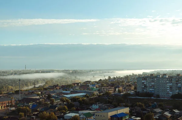 Morning mist over the river flowing in the city and blue cloudy sky from above, aerial view.