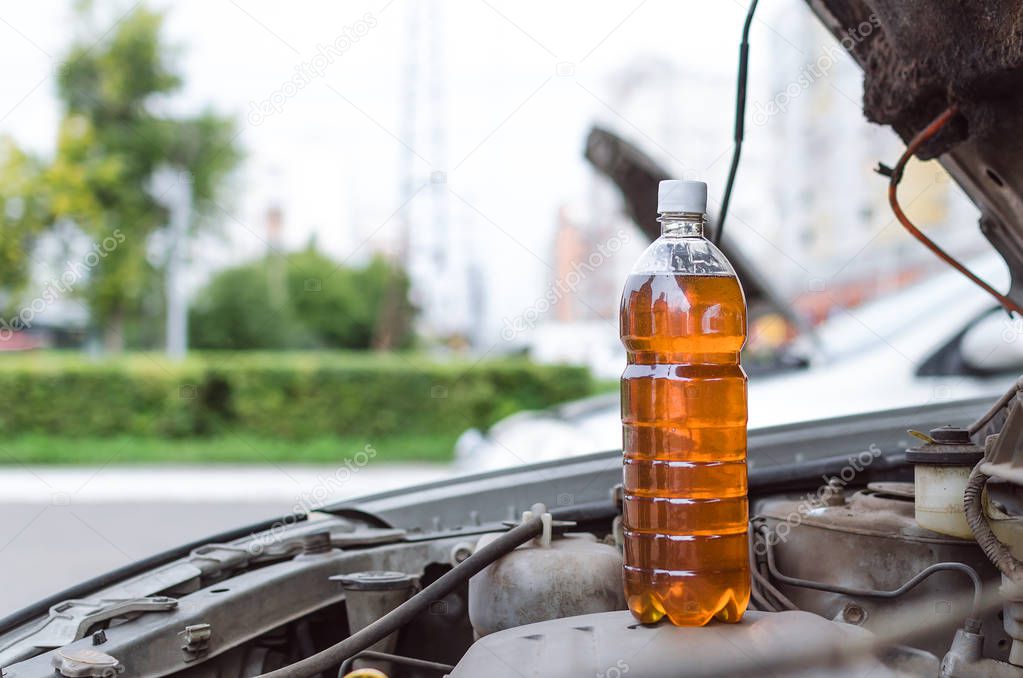 Bottle of new motor oil standing on open car hood.