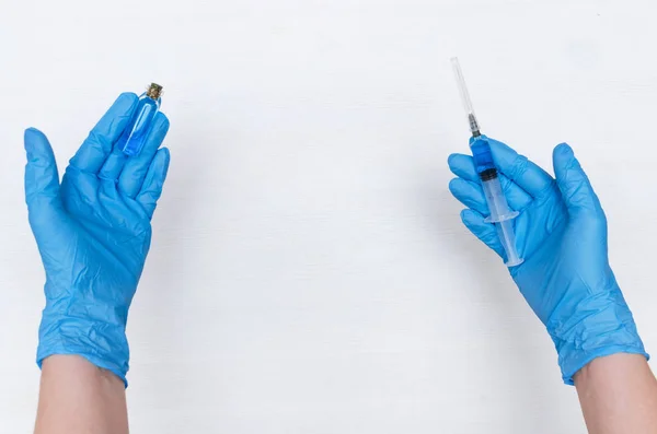 Nurse is holding in hand a syringe with blue liquid medicine on the doctor table background.