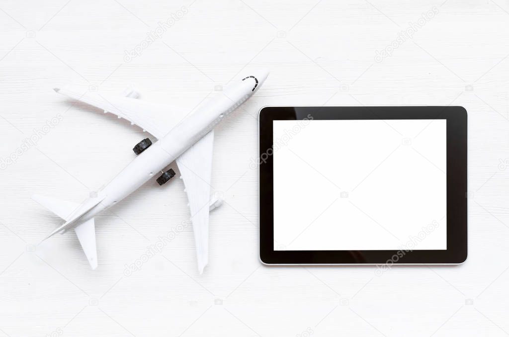 Toy airplane and mobile tablet computer with blank screen on white wooden table background.