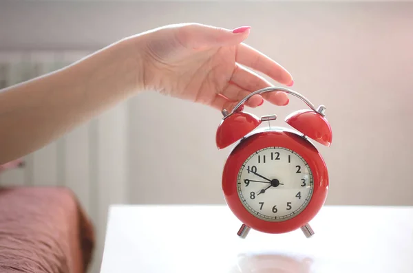 睡在床上的昏昏欲睡的女人在手拿着一个红色的闹钟在上午时间 — 图库照片