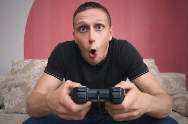 Şaşırdım ve hevesli oyun adam elinde bir joystick ile geniş açık ağızlı bir kanepede oturuyor ve video oyun oynuyor. Heyecan verici oyun kavramını