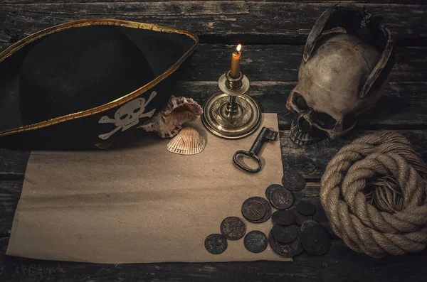 Pirate treasure map with copy space, pirate captain hat, coins, human skull, seashells, mooring rope and burning candle. Treasure hunter concept background.