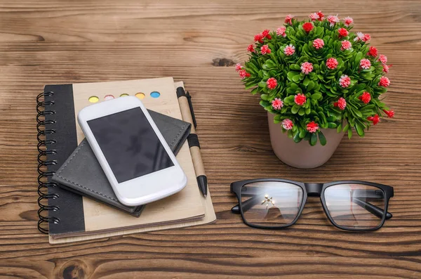 Different accessories on the office table. Mobile phone with blank screen, glasses, notepad with a pen and wallet. Business background.